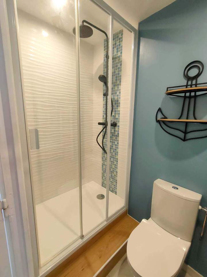 Cabine de douche avec une étagère murale en forme d'ancre et une toilette, installées dans une petite salle de bains, Yvelines
