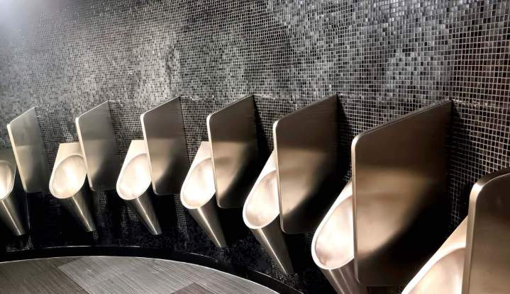 Rangée d'urinoirs publics en acier inoxydable installés le long d'un mur carrelé de mosaïque noire, Yvelines 